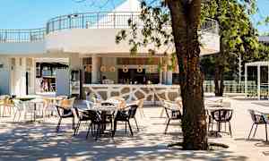 En udendørsbar med borde og stole under træer med lys indretning og træelementer. (AI-genereret tekst)