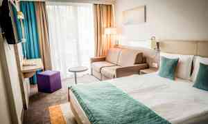 Et moderne hotelværelse med en dobbeltseng, sofa og vindue med gardiner. (AI-genereret tekst)