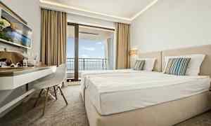 Hotelværelse med to senge, skrivebord og altan med havudsigt. (AI-genereret tekst)