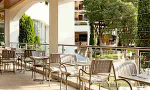 Et udendørs serveringsområde med borde og stole, omgivet af grønne træer og beplantninger. (AI-genereret tekst)