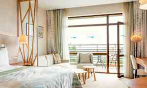 Et hotelværelse med seng, siddeområde, bord og åben altandør. (AI-genereret tekst)