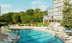 En pool omgivet af liggestole og parasoller nær et hotel med flere etager. (AI-genereret tekst)