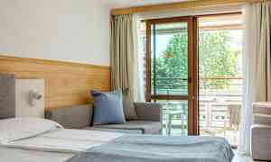 Et hotelværelse med en seng, sofa og altanmøbler synlige gennem en glasdør. (AI-genereret tekst)