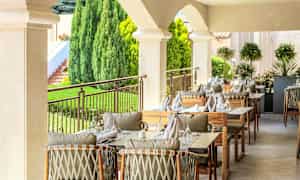 Udendørs servering med dækkede borde og stole i en frodig omgivelser. (AI-genereret tekst)