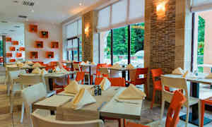 Fotografi af en indendørsrestaurant med dækkede borde og stole i forskellige farver. (AI-genereret tekst)