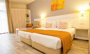 Et lyst hotelværelse med to senge, orange detaljer og møbler. (AI-genereret tekst)