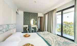 Hotelværelse med lyse møbler og store vinduer med udsigt over havet. (AI-genereret tekst)