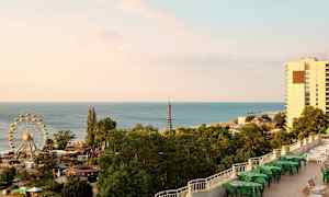 Billedet viser en kyst med havet, et pariserhjul, frodige træer og bygninger. (AI-genereret tekst)