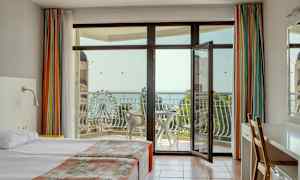 Hotelværelse med dobbeltseng, åben altandør og udsigt over havet og et pariserhjul. (AI-genereret tekst)