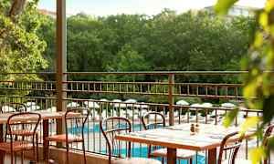 Udendørs servering med borde og stole samt udsigt over poolområde og grøntområder. (AI-genereret tekst)