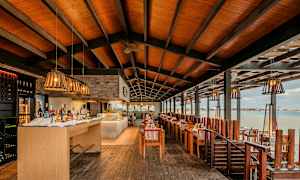 Restaurant ved vandet med dækkede borde, træinteriør og loftsdekorationer. (AI-genereret tekst)
