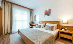 Et hotelværelse med en dobbeltseng, en skrivebordsstol, et vindue med gardiner og en vægdekoration. (AI-genereret tekst)