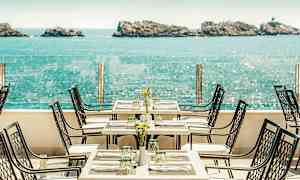 En restaurantterrasse med havudsigt, borde og stole er opstillet med borddækning. (AI-genereret tekst)