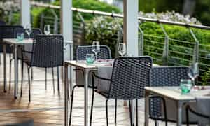 En udendørs servering med borde og stole dækket med glas og servietter. (AI-genereret tekst)