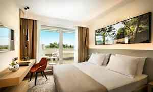 Hotelværelse med en seng, skrivebord og stol samt en balkon med havemøbler. (AI-genereret tekst)