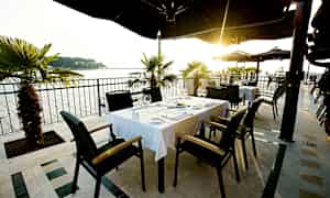 Udendørs serveringsområde med borde og stole, med havudsigt og solnedgang. (AI-genereret tekst)