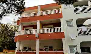 Lejlighedsbygning med altaner og vinduer, omgivet af planter. (AI-genereret tekst)