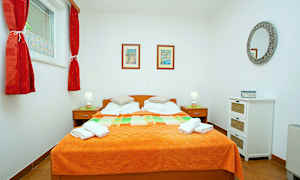 Et soveværelse med en dobbeltseng og orange sengetæppe, to sengeborde med lamper og vægdekorationer. (AI-genereret tekst)