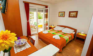 Et værelse med en dobbeltseng, bord, stole og en åben altandør. (AI-genereret tekst)