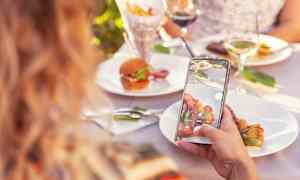 Person tager foto af tallerken med mad på udendørs bord. (AI-genereret tekst)