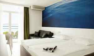 Dobbeltværelse med stort blåt vægmaleri bag sengen. Altan med havudsigt. (AI-genereret tekst)