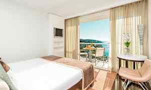 Hotelværelse med en stor seng, der vender ud mod en balkon med udsigt over havet. (AI-genereret tekst)