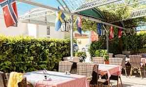 Udendørsterrasse med borde, stole og flag, omgivet af grønt. (AI-genereret tekst)