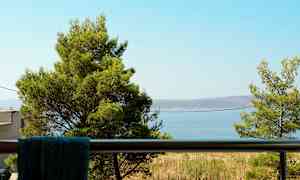 Udsigt fra en balkon med træer og havet i baggrunden. (AI-genereret tekst)