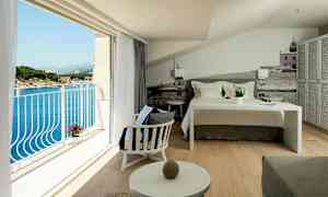 Et hotelværelse med en redt seng, siddeområde og en altan med udsigt over havet. (AI-genereret tekst)