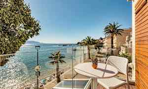 Udsigt fra en altan mod en solrig strand med palmer og klart vand. (AI-genereret tekst)