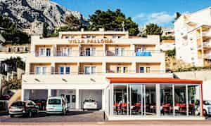 En bygning med teksten 'Villa Palloma' øverst, med altaner og parkerede biler foran. (AI-genereret tekst)