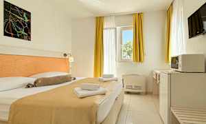 Et hotelværelse med en dobbeltseng, lyse gardiner og møbler samt et vindue, der slipper dagslys ind. (AI-genereret tekst)