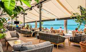 Udendørs servering med borde og sofaer, udsigt over havet i baggrunden. (AI-genereret tekst)