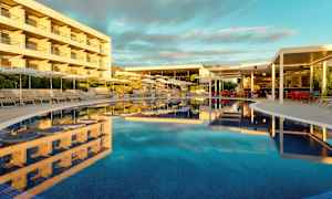 En pool omgivet af liggestole og parasoller ved siden af en bygning og en restaurant. (AI-genereret tekst)