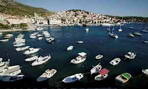 En kystby med små både i en havn og bygninger i baggrunden. (AI-genereret tekst)