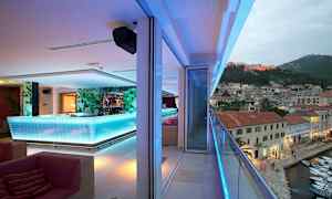 En moderne bar med en lys bardisk indendørs og en altan med udsigt over en lille by og havn. (AI-genereret tekst)