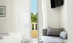 Et hotelværelse med en sofa, en seng og en altandør, der fører ud til udsigt over træer. (AI-genereret tekst)