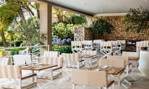 En udendørs terrasse med borde, stole og en stenmur. (AI-genereret tekst)