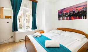 Et soveværelse med dobbeltseng, turkise gardiner og et billede af en bysilhuet på væggen. (AI-genereret tekst)