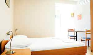 Et simpelt hotelværelse med en seng af træ, et natbord og et bord med to stole. (AI-genereret tekst)