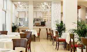 En restaurant med borde og stole, dekoreret med planter og en glasvæg med et træsdesignmotiv. (AI-genereret tekst)