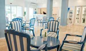 En lys og luftig hotellobby med blå og hvidstribede møbler og et rundt bord. (AI-genereret tekst)