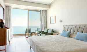 Hotelværelse med seng, siddegruppe og udsigt til havet gennem glasdøre. (AI-genereret tekst)