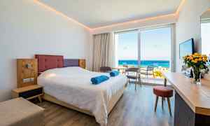 Hotelværelse med en dobbeltseng, siddegruppe og udsigt over havet. (AI-genereret tekst)