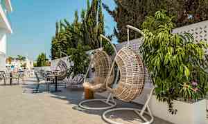 Hængende kurvestole og borde på en terrasse med planter og parasoller. (AI-genereret tekst)