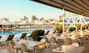 Poolområde med liggestole, parasoller og spiseborde ved vandet. (AI-genereret tekst)