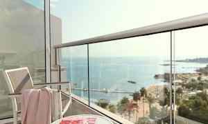 Udsigt fra en altan mod havet, med en stol, et bord og et magasin. (AI-genereret tekst)