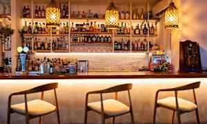 En bardisk med stole og hylder fyldt med flasker og glas. (AI-genereret tekst)