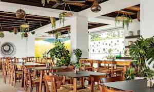 Restaurant med træborde og stole, dekoreret med grønne planter. (AI-genereret tekst)