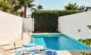 En mindre pool omgivet af hvide vægge og grøn vegetation, med to solsenge nær kanten. (AI-genereret tekst)